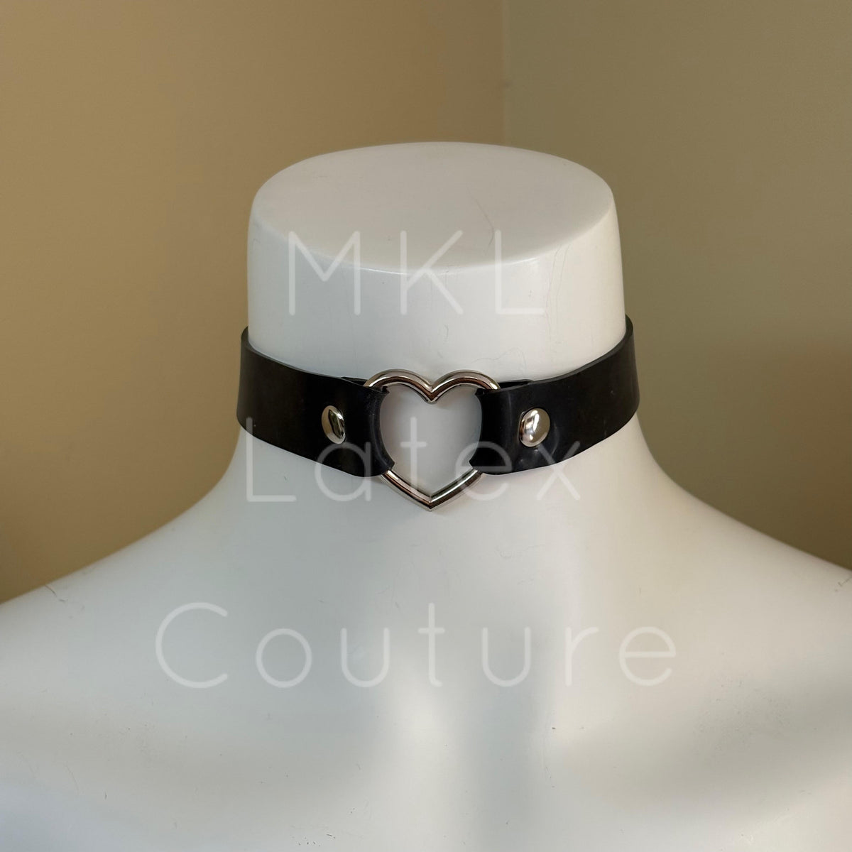 Heavy latex choker with a central metal heart shape secured in place by studs with a back buckles with 4 eyelets for adjustment.