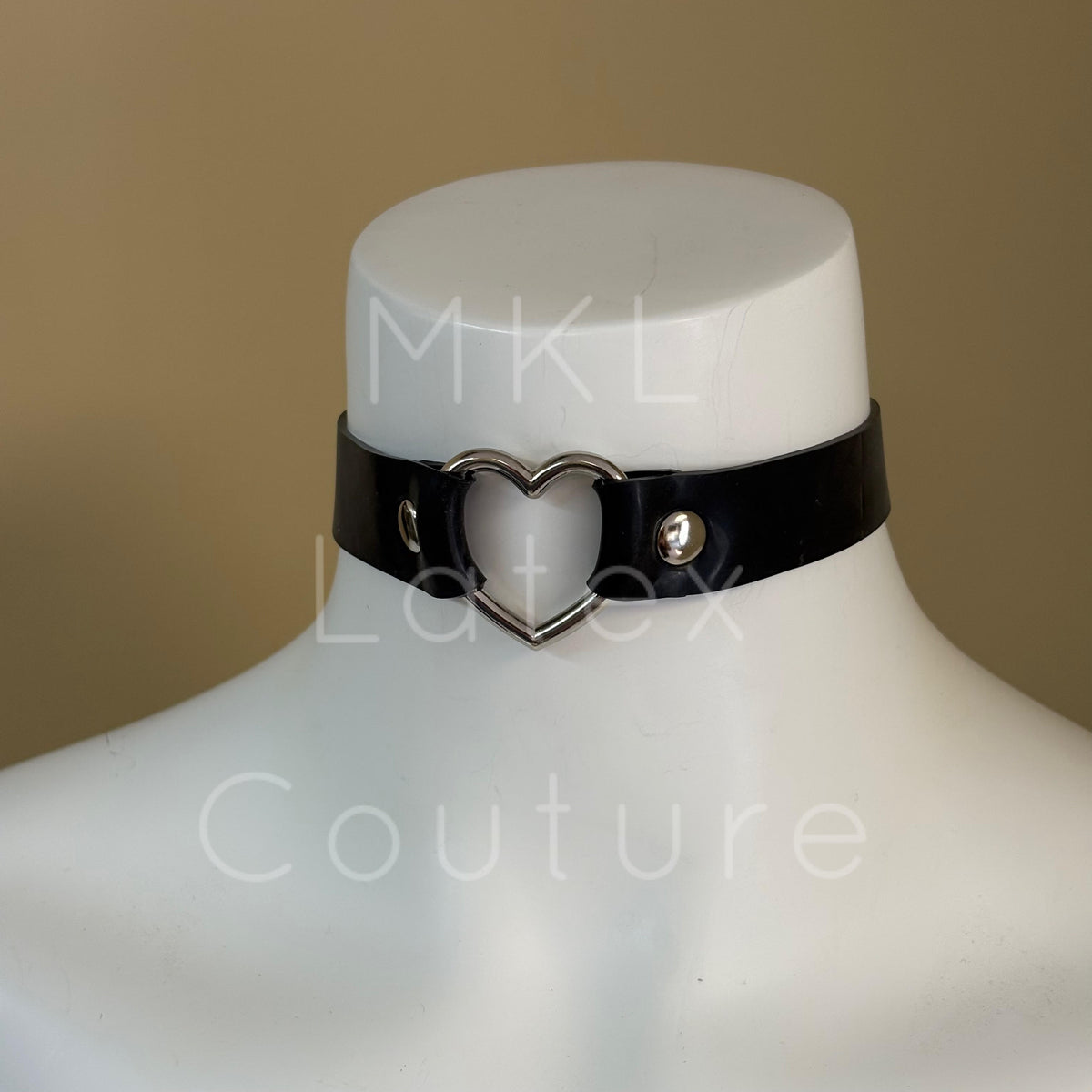 Heavy latex choker with a central metal heart shape secured in place by studs with a back buckles with 4 eyelets for adjustment.